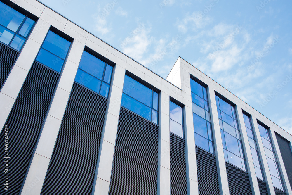 Fototapeta premium Modern glass office building facade on a sunny day under bright blue sky with white clouds. Big city life, contemporary architecture, offline business style background.