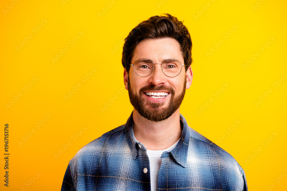 Obraz premium Smiling bearded man wearing glasses and plaid shirt against bright yellow background, casual portrait showing happiness and confidence