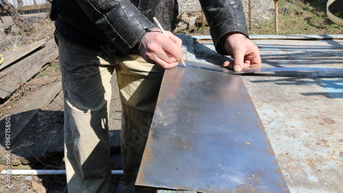 marking and checking the required size on a small sheet of metal lying on the work surface in an outdoor craft workshop using a pencil and ruler in the hands of a craftsman, marking an iron plate