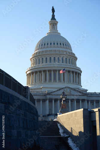 Last beams of golden sunlight on the United States Capitol Building in Washington, DC, with the American flag waving, blue sky backrgound