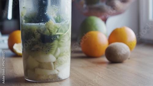 lose-up of a blender processing fresh fruits into a smooth, creamy smoothie in a glass container. Ingredients like kiwi, banana, and green leaves are being blended into a healthy drink.