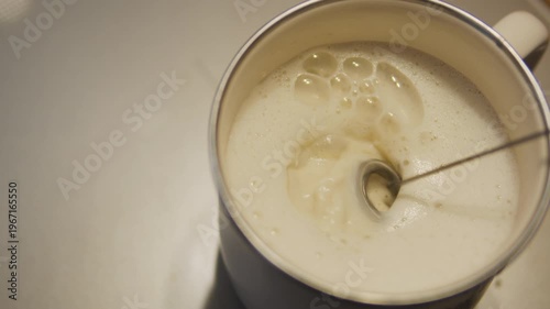 Top view of milk frothing with blender in metal cup. Coffee making process, homemade latte or cappuccino, barista concept.