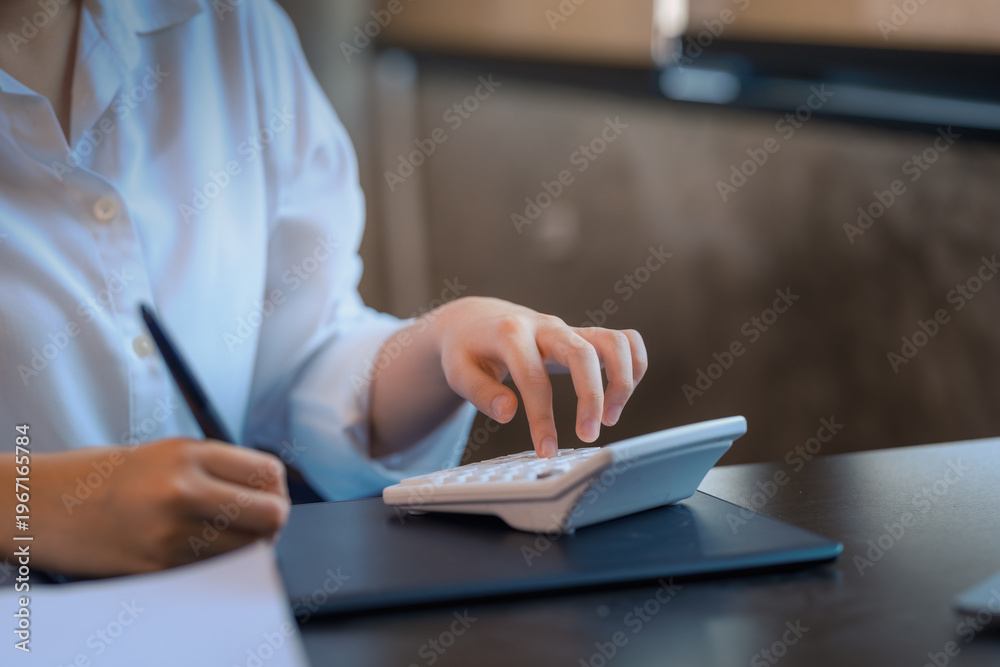 Fototapeta premium Close-up of businesswoman hands using calculator and writing on notebook at office desk.