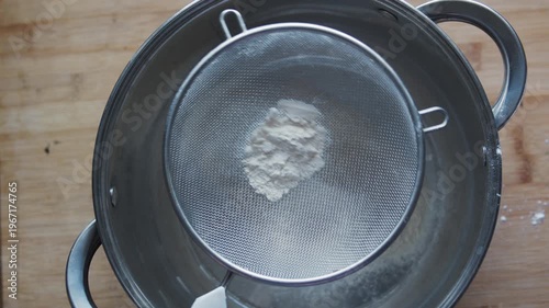 Top view of flour sifting through sieve on table, baking preparation. Overhead shot of dough making for bread and pastry, homemade kitchen scene, cooking concept.