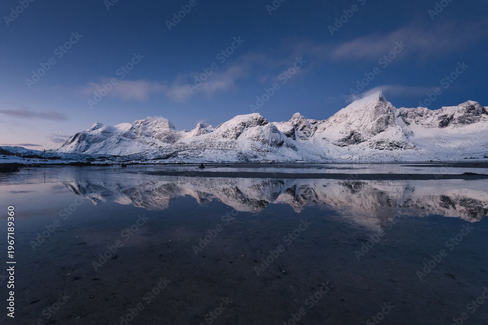 Obraz premium Spectacular view of winter Lofoten at sunset. Rugged, snow-capped mountains rising straight from the icy Norwegian Sea. Arctic light highlighting the dramatic beauty of wild Nordic nature.