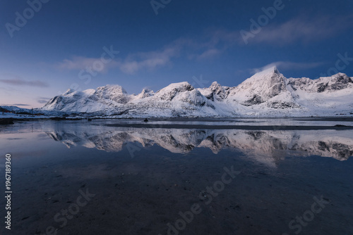 Spectacular view of winter Lofoten at sunset. Rugged, snow-capped mountains rising straight from the icy Norwegian Sea. Arctic light highlighting the dramatic beauty of wild Nordic nature.
