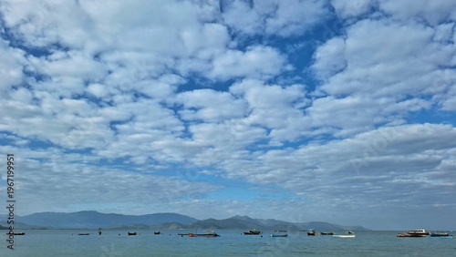 Canvas Print A view of the beach with a blue sky scattered with white clouds and several fishing boats parked