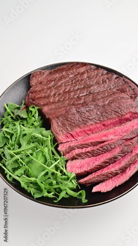 Cooking a beef steak with fresh arugula on a black plate prepared for a meal in a kitchen