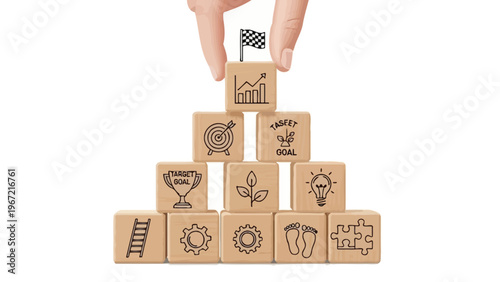 A hand placing a block with a graph on top of a pyramid of wooden blocks with various business and goal-oriented symbols