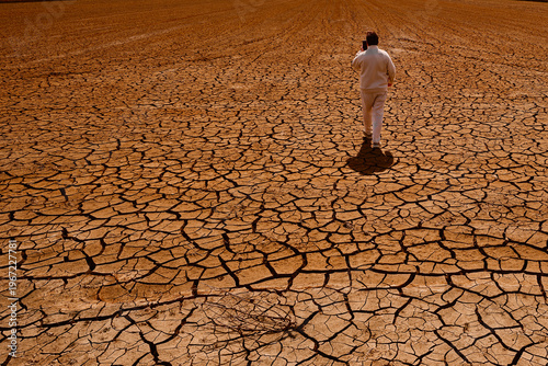 Картината върху платно Man walking across cracked dry ground in a dried landscape during drought
