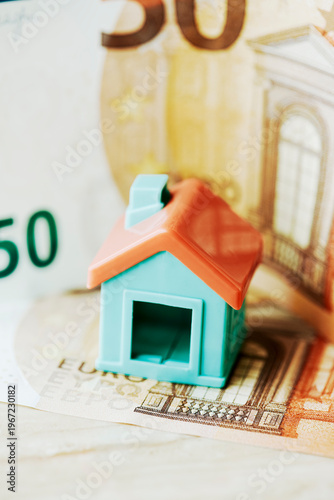 a toy house placed over a euro banknote