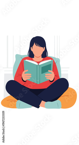 A person with dark hair sits cross-legged while reading a book on soft cushions