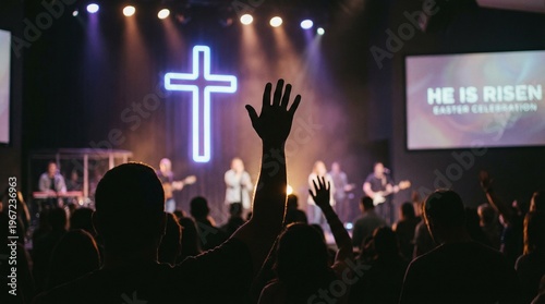 Silhouetted hand raised in worship before a glowing neon cross. Christian concert prayer service at church. Spiritual praise and adoration during Easter Sunday worship celebration. 