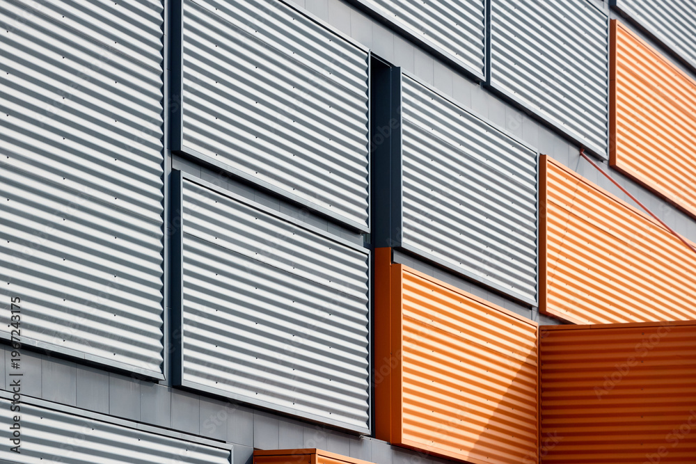 Fototapeta premium Architectural facade with orange cladding corrugated metal panels, large glass window of industrial or commercial building, contemporary architecture with vertical relief and material contrast.