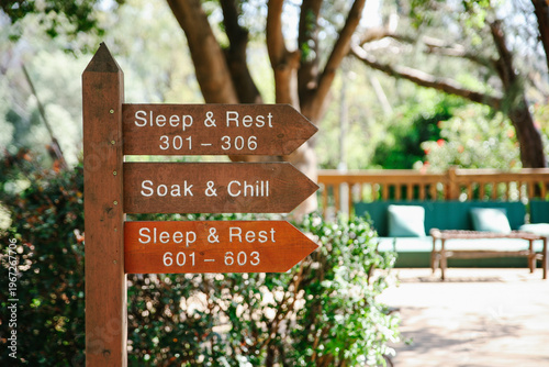 Close-up of a Wooden Directional Signpost for Sleep, Rest, and Chill Areas in a Sunlit Outdoor Resort Garden with a Soft Bokeh Background