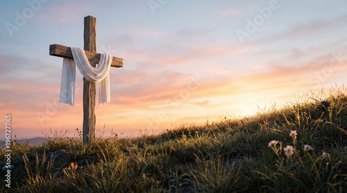 A wooden cross stands on a grassy hill with a white cloth draped over it at sunset