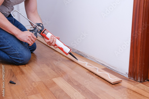 Konstfotografi Man applying adhesive with caulking gun for baseboard installation