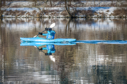 Kayaker paddling on calm river with reflection in winter landscape