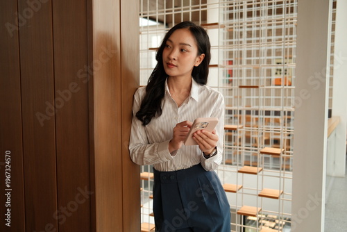 Young asian businesswoman looking away holding smartphone