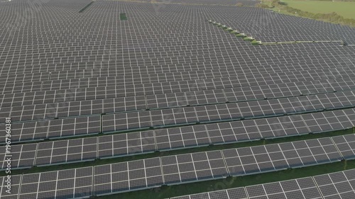 Aerial drone video of a large solar panel field at an energy company facility. Rows of photovoltaic panels capture sunlight to generate clean electricity, representing renewable energy, sustainability