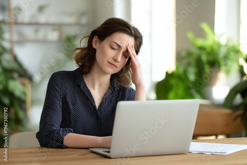 Woman looks worried while working on a laptop in a bright room