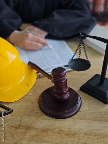 Construction worker reviews legal documents while sitting at a desk with a gavel, scale, and safety helmet concept