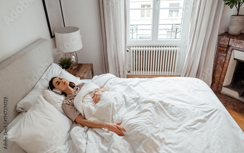Woman in bed with headphones listening to meditation or relaxing sleep music