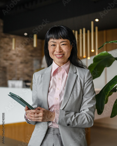 Asian businesswoman smiling holding tablet in modern office
