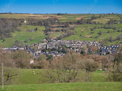 Wide view of Pateley Bridge in Yorkshire UK, with stone houses set among green fields and rolling hills under a clear blue sky