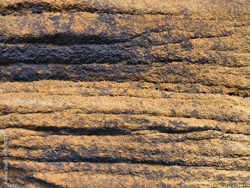 Warm light reveals the rough layered surface of millstone grit in Yorkshire UK, creating a natural abstract rock texture background