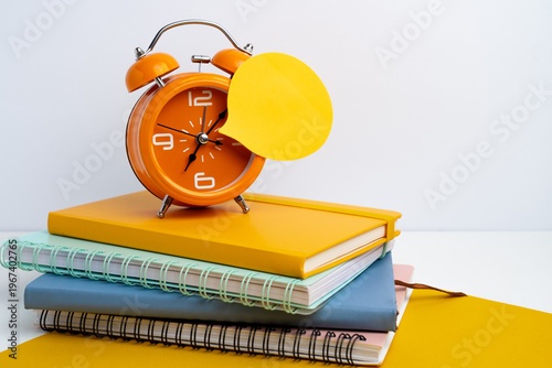 Orange alarm clock with yellow speech bubble sticker on bright yellow background. Time management and reminder concept. 