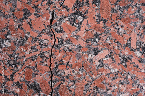 Polished natural stone surface or granite slab with red, grey, white, and black mineral patterns. The crack running across the background.