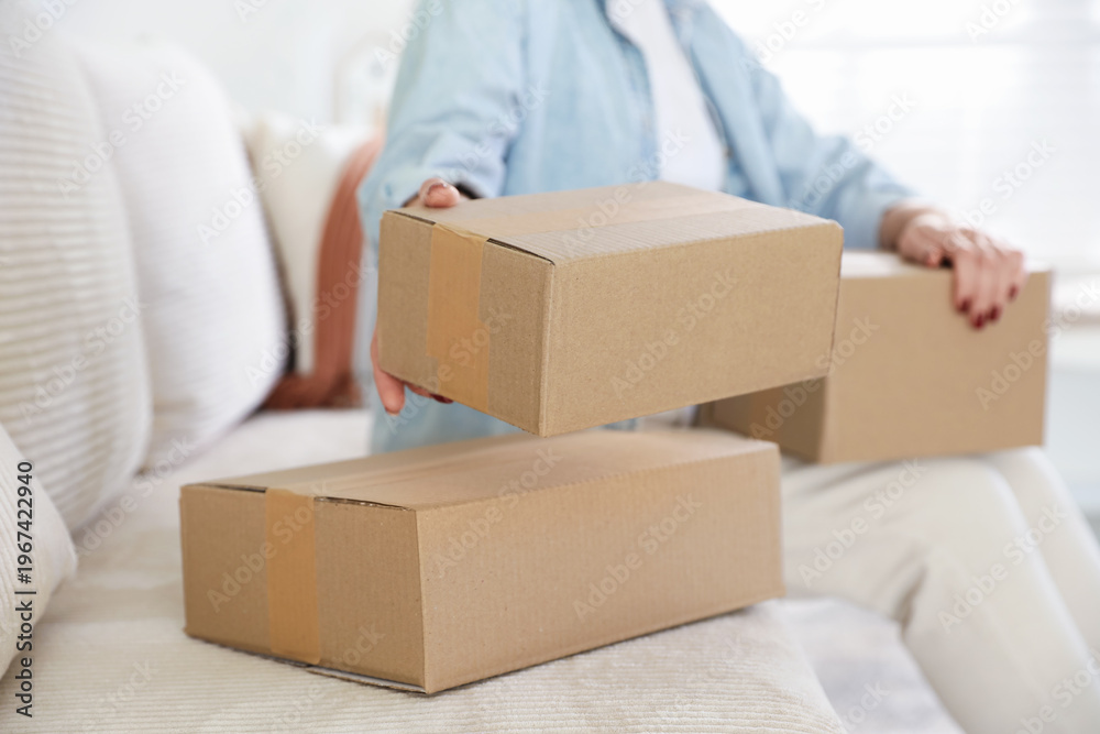 Fototapeta premium Parcel delivery. Woman with cardboard boxes on sofa at home, closeup
