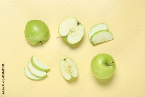 Whole and cut fresh apples on pale yellow background, flat lay