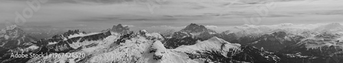 Black and white panoramic view of snow covered Dolomites mountain range with dramatic clouds