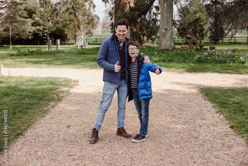 Father and son showing thumbs up standing together outdoors in park