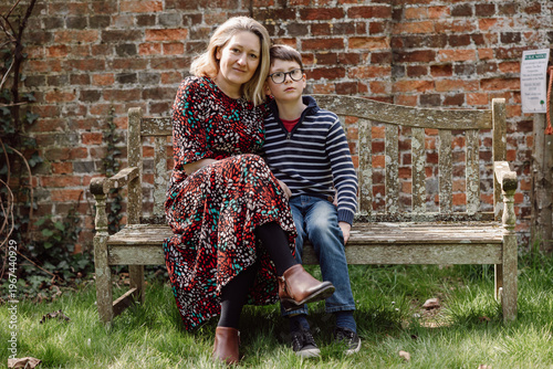 Mother and son sitting on bench together outdoors in front of brick wall