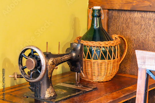 Фотография Vintage antique black sewing machine with gold ornaments and large glass wine ca
