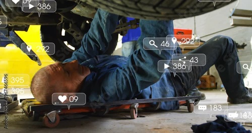 Mechanic lying on creeper torquing bolts for repair, with views rising, alerts appearing over wheel