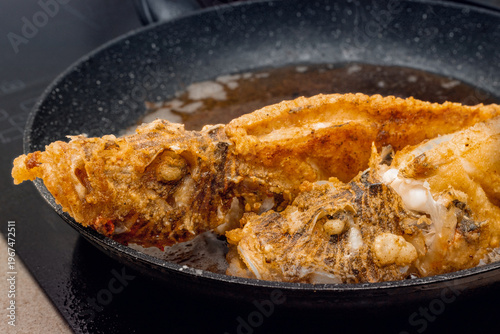 Very tasty fried sea fish on a frying pan, with a flour coating