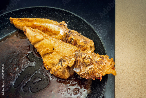 Very tasty fried sea fish on a frying pan, with a flour coating