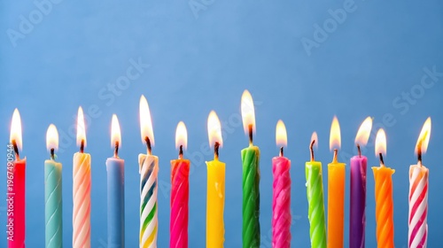Colorful Candles With Flames Arranged in a Line on a Blue Surface for Celebra...