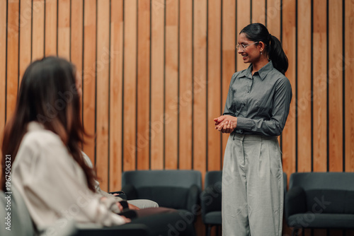 Woman standing and smiling while presenting to a seated audience at a seminar or business meeting, communicating ideas