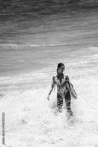 A beautiful girl surfs in a jumpsuit in the middle of the ocean waves