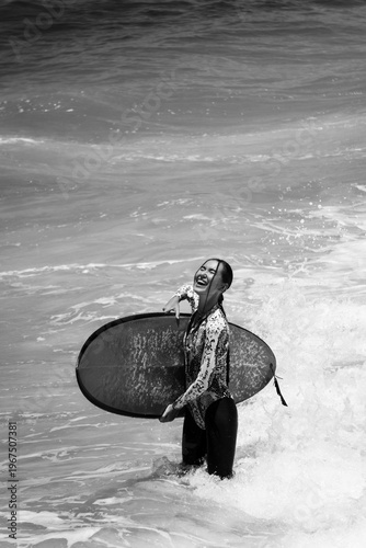 A beautiful girl surfs in a jumpsuit in the middle of the ocean waves