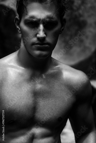 Portrait of a shirtless man among rocks near a waterfall, black and white photograph