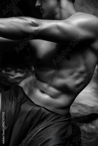 Portrait of a shirtless man among rocks near a waterfall, black and white photograph