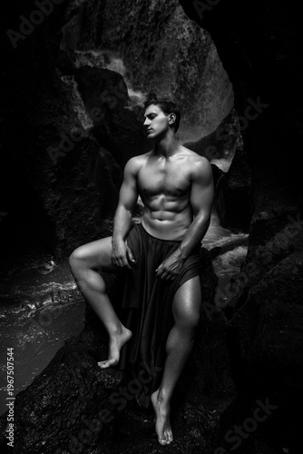 Portrait of a shirtless man among rocks near a waterfall, black and white photograph