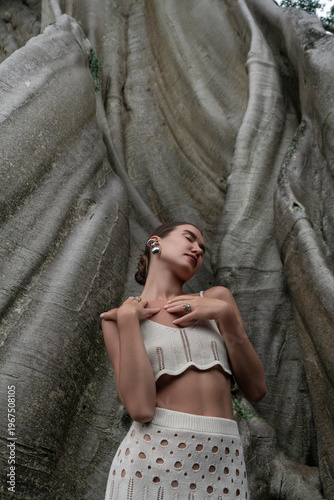 A beautiful girl in an elegant dress poses near an old tree