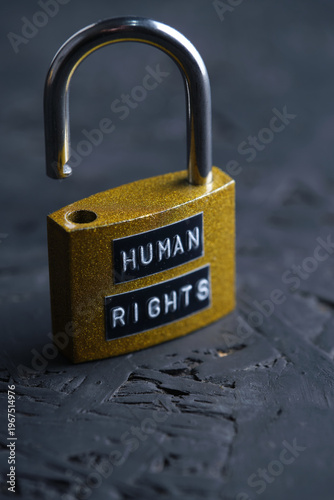 An open yellow padlock with the words Human Rights on dark textured background, representing freedom and liberation.